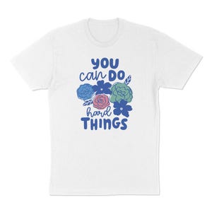 Puede incluir: Camiseta blanca con la frase "YOU can DO hard THINGS" en azul y ilustraciones florales en azul, verde y rosa. Una camiseta motivacional para el d&iacute;a a d&iacute;a.