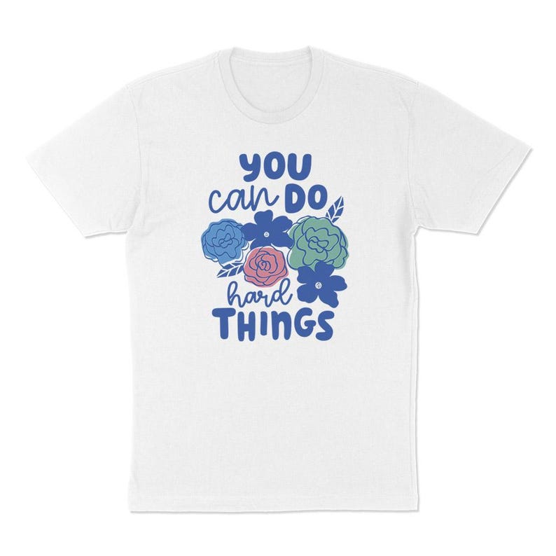 Puede incluir: Camiseta blanca con la frase "YOU can DO hard THINGS" en azul y ilustraciones florales en azul, verde y rosa. Una camiseta motivacional para el d&iacute;a a d&iacute;a.