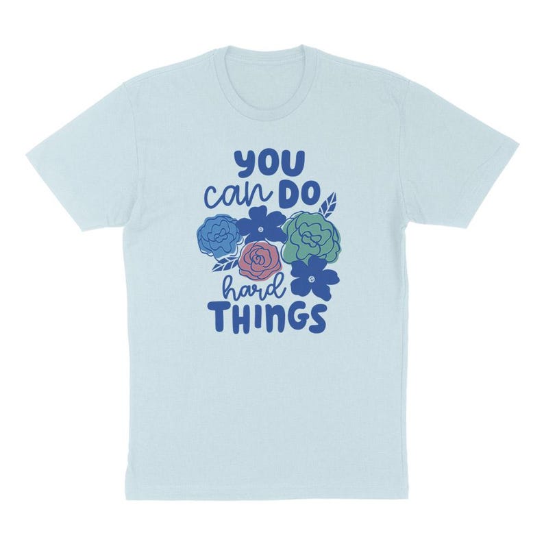 Puede incluir: Camiseta azul claro con el texto "YOU can DO hard THINGS" en azul. El dise&ntilde;o incluye un grupo de flores coloridas en azul, rosa y verde. La camiseta est&aacute; hecha de un material suave.