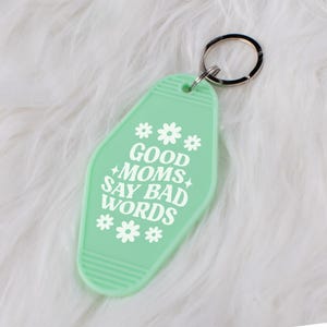 May include: A light green motel key chain with the text "GOOD MOMS SAY BAD WORDS" in white. The keychain has a white flower design at the top and bottom.