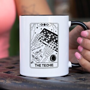 May include: White ceramic mug with a black interior and handle. The mug features a tarot card-style design with a skeleton typing on a keyboard, roses, and the text "THE TECHIE" and "NEVER LOGGED OFF".