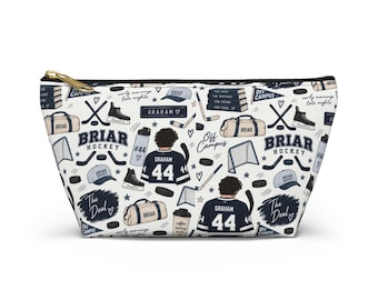 May include: A white zippered pouch featuring a repeating pattern of Briar Hockey themed illustrations including hockey jerseys with the name Graham and number 44, hockey sticks, pucks, goals, duffel bags, water bottles, and the text Off Campus.