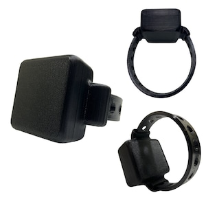 Op de afbeelding: Zwarte plastic enkelband met een vierkant apparaat. De armband is verstelbaar en heeft een reeks gaten om de band vast te maken.