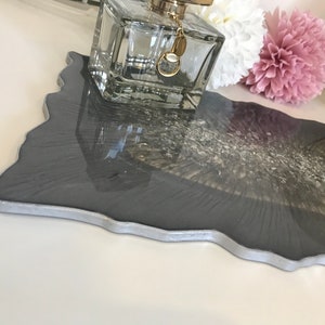 May include: A grey resin tray with a silver edge and a white and silver marbled design. The tray is shaped like a large leaf and has a glossy finish.
