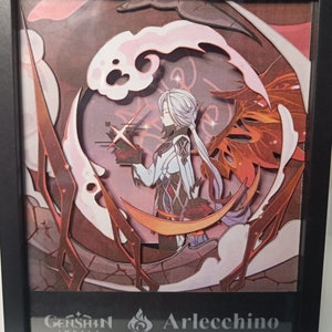 Könnte beinhalten: Ein Papierkunstwerk mit einer Figur aus dem Videospiel Genshin Impact. Die Figur, Arlecchino, ist in einem weißen und schwarzen Outfit mit einem roten und orangen Hintergrund dargestellt. Das Kunstwerk ist in Schwarz gerahmt.
