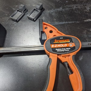 K&ouml;nnte beinhalten: Eine orangefarbene Jorgensen E-Z Hold 6 Zoll Klemme mit einer schwarzen Metallstange und schwarzen Kunststoffpolstern. Die Klemme hat eine maximale Klemmkraft von 136 kg.