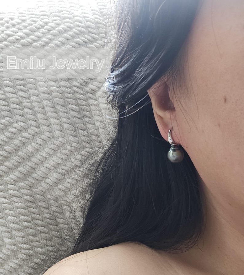 May include: A pair of silver hoop earrings with a single black pearl dangling from each hoop.