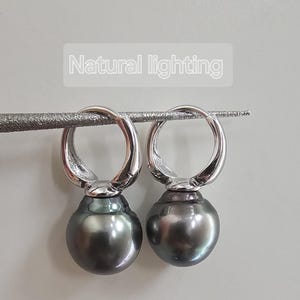 May include: A pair of silver hoop earrings with a dark grey pearl dangling from each hoop.