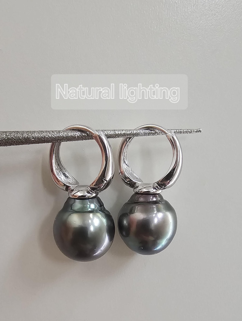 May include: A pair of silver hoop earrings with a dark grey pearl dangling from each hoop.