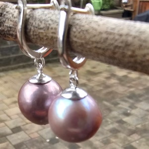 May include: A pair of silver hoop earrings with a dangling iridescent purple pearl on each earring.