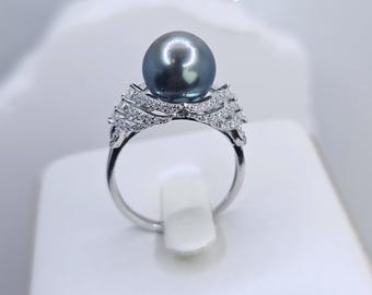 Könnte beinhalten: Ein silberner Ring mit einem großen schwarzen Perlmutt und einem filigranen, komplizierten Design aus kleinen Diamanten. Der Ring wird auf einer weißen Ringbox präsentiert.