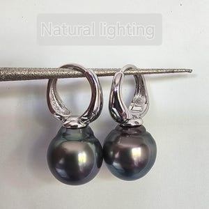 May include: A pair of silver hoop earrings with a dark gray pearl drop. The earrings are hanging from a white surface.