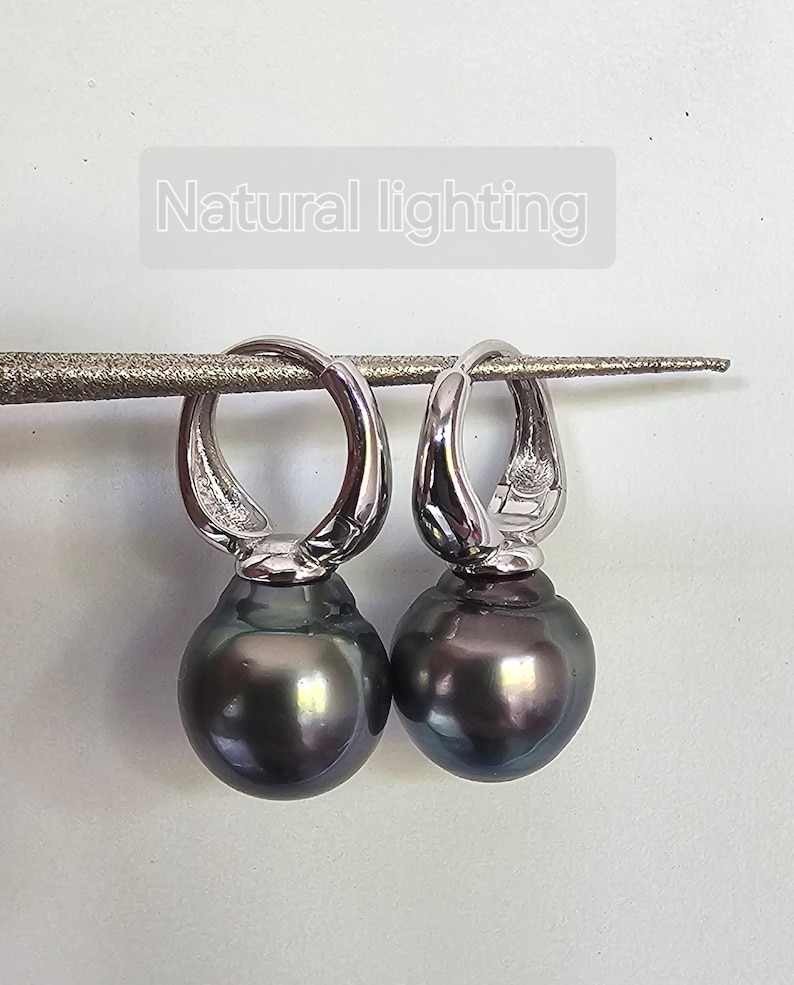 May include: A pair of silver hoop earrings with a dark gray pearl drop. The earrings are hanging from a white surface.