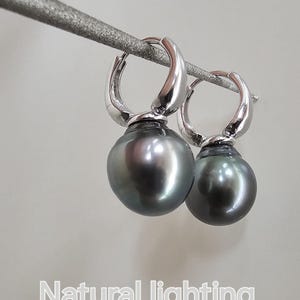 May include: A pair of silver hoop earrings with a black pearl dangling from each hoop. The earrings are photographed against a white background with natural lighting.