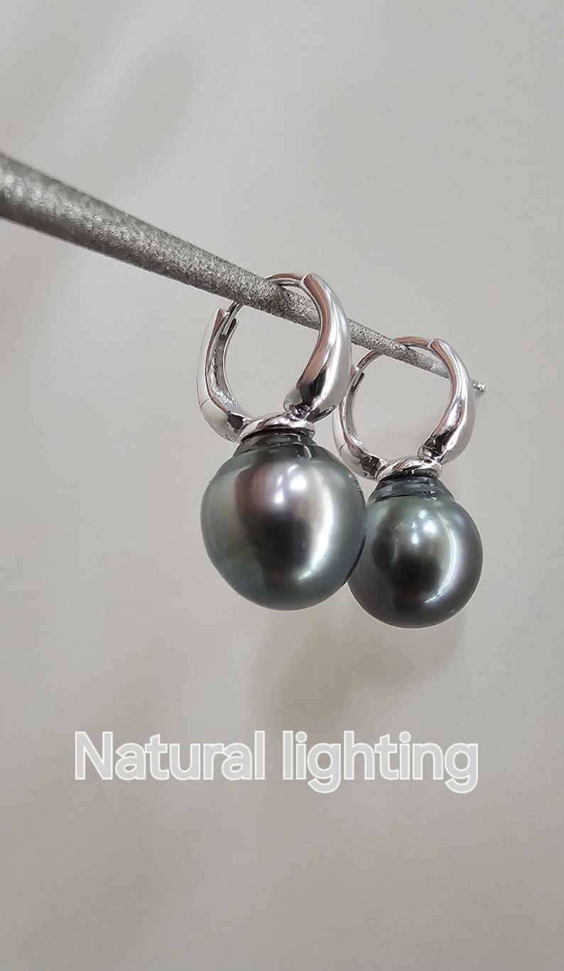 May include: A pair of silver hoop earrings with a black pearl dangling from each hoop. The earrings are photographed against a white background with natural lighting.