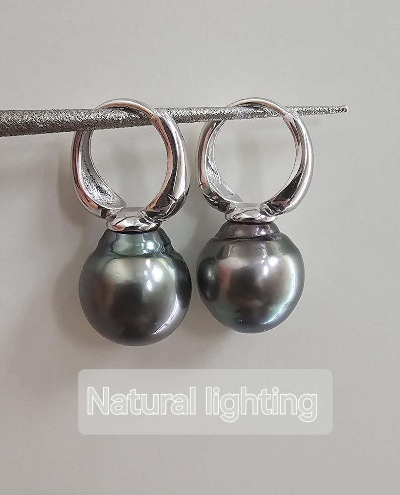 May include: A pair of silver hoop earrings with black pearl drops. The earrings are photographed on a white surface with natural lighting.