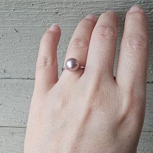 May include: A silver ring with a single, large, round, light pink pearl.