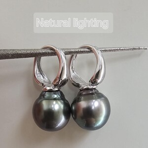 May include: A pair of silver hoop earrings with a dark grey pearl dangling from each hoop.  Natural lighting.