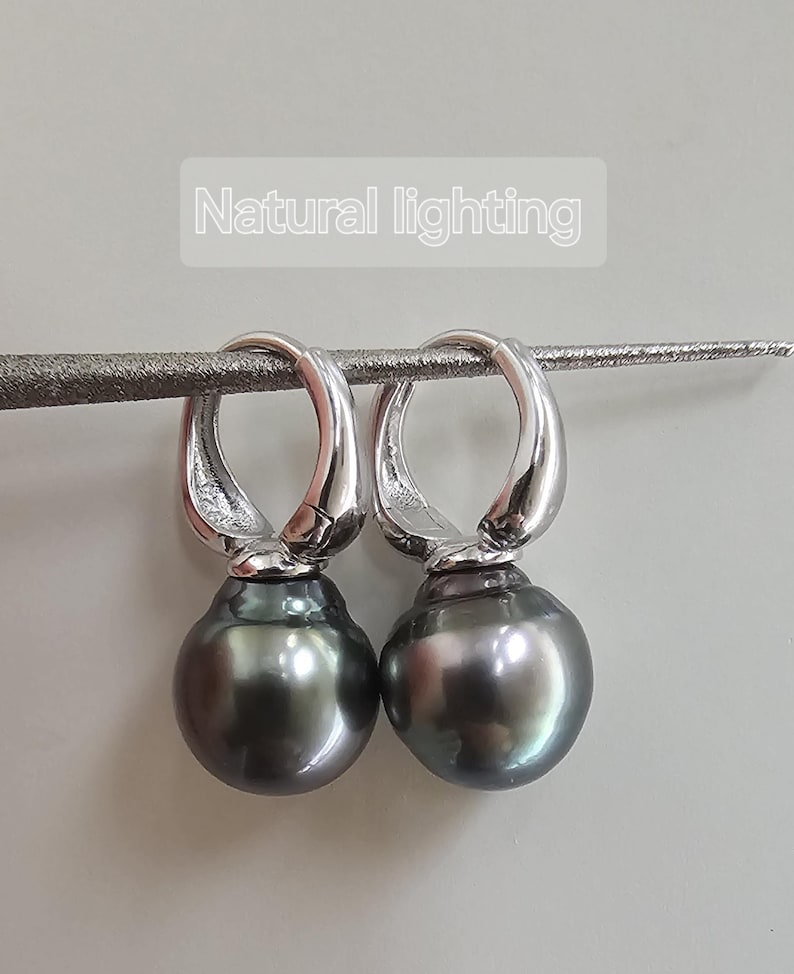 May include: A pair of silver hoop earrings with a dark grey pearl dangling from each hoop.  Natural lighting.