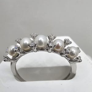 Puede incluir: Un anillo de plata con una fila de perlas y pequeños diamantes engastados en el metal.