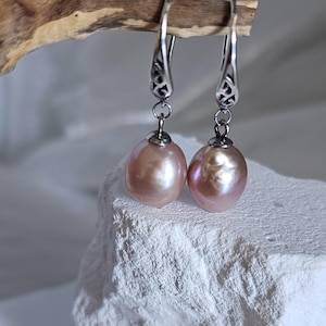 May include: A pair of elegant drop earrings featuring lustrous, peach-colored freshwater pearls. The earrings have ornate silver-toned hooks with decorative detailing. The pearls are approximately 0.75 inches in length, suspended from the hooks.