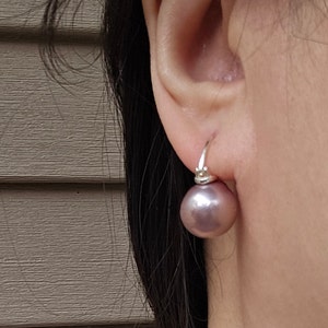 May include: A pair of silver hoop earrings with a single, large, round, lavender pearl dangling from each hoop.