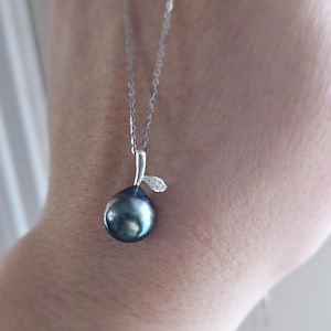 May include: A silver chain necklace with a black pearl pendant. The pendant is shaped like a pear and has a small silver leaf with a diamond accent.