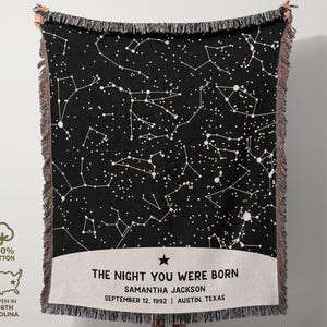 May include: Black woven throw blanket featuring a white constellation design. The blanket has a cream-colored band with the text "THE NIGHT YOU WERE BORN" and a name, date, and location. The blanket is made of 100% cotton and woven in North Carolina.