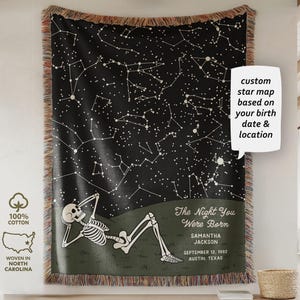 May include: A black woven throw blanket featuring a custom star map design. The blanket displays a skeleton relaxing under a starry night sky. Text includes "The Night You Were Born" and a birthdate. Made of 100% cotton and woven in North Carolina.