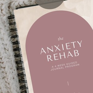Könnte beinhalten: Ein rosa und cremefarbenes Journal mit dem Titel "the ANXIETY REHAB" und dem Text "A 4 WEEK GUIDED JOURNAL PROGRAM" und "a journal from LAURIE WILLIAMS DIGITAL WIFE SUCCESS".
