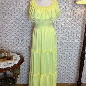 May include: A yellow maxi dress with a ruffled neckline and lace trim. The dress has a tiered skirt and is made of a lightweight fabric.