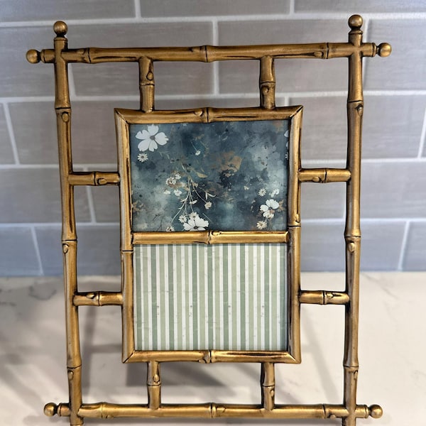 May include: A gold-colored metal picture frame with a faux bamboo design. The frame features a rectangular central opening containing a two-part insert: the top half displays a dark blue floral pattern, and the bottom half shows light green vertical stripes.