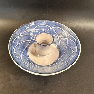 May include: A ceramic serving dish with a blue and white abstract design. The dish has a circular base with a raised center and a wide, shallow bowl. The blue design features intersecting lines, and the rim is white.