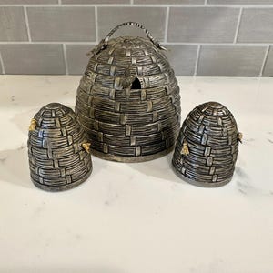 May include: A set of three silver beehive-shaped salt and pepper shakers with gold accents. The shakers are made of metal and have a textured surface.