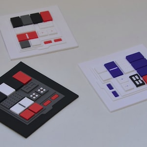 Può includere: Tre piastrelle quadrate bianche con pulsanti di diversi colori. La prima piastrella ha pulsanti rossi, neri e grigi. La seconda piastrella ha pulsanti blu, bianchi e neri. La terza piastrella ha pulsanti rossi e neri.