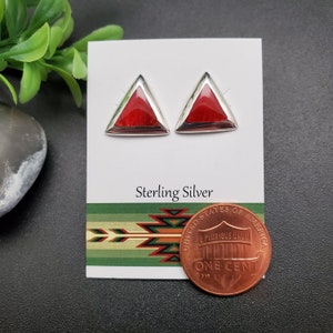 May include: A pair of sterling silver earrings with red triangular stones. The earrings are displayed on a white card with the words "Sterling Silver" printed on it. A penny is included for size reference.
