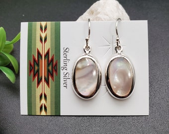 May include: A pair of sterling silver earrings with oval-shaped mother-of-pearl stones. The earrings are on a white card with the words "Sterling Silver" printed on it.