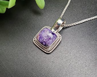 Peut inclure: Un collier avec un pendentif en argent en forme de carré avec une pierre précieuse violette et blanche sertie dans une bélière en argent. Le pendentif a une bordure en argent détaillée.
