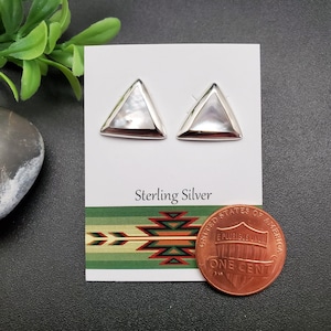May include: A pair of sterling silver earrings with a triangular shape and a mother-of-pearl inlay. The earrings are displayed on a white card with the words "Sterling Silver" printed on it. A penny is included for size reference.