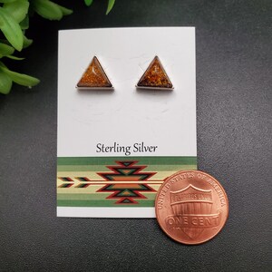 May include: A pair of sterling silver triangle earrings with amber stones. The earrings are displayed on a white card with the words "Sterling Silver" printed on it. A penny is also included in the image for size reference.