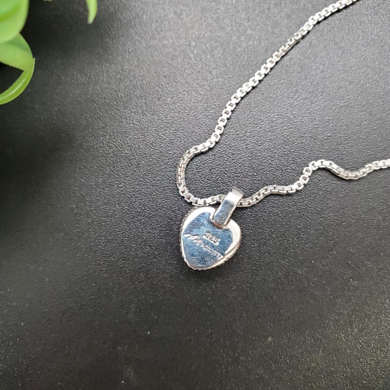 May include: A silver heart-shaped pendant necklace with a silver chain. The back of the pendant has the inscription "925 Italy" on it.