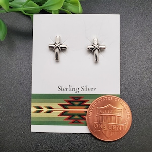 Può includere: Un paio di orecchini a perno a croce in argento sterling, mostrati su una carta bianca con le parole "Sterling Silver" stampate su di essa. Un centesimo è incluso per il confronto delle dimensioni.