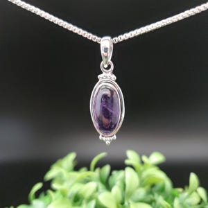 May include: A silver chain necklace with a pendant featuring a purple oval gemstone set in a silver bezel.