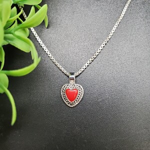 May include: A silver chain necklace with a red heart pendant. The heart pendant has a silver filigree design around the edge.