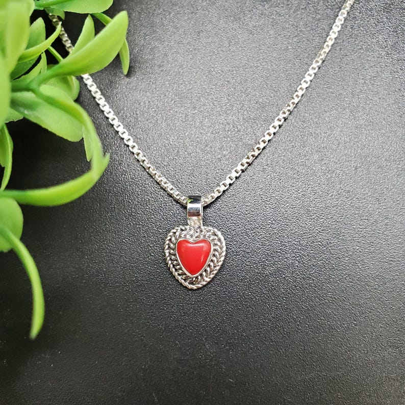 May include: A silver chain necklace with a red heart pendant. The heart pendant has a silver filigree design around the edge.