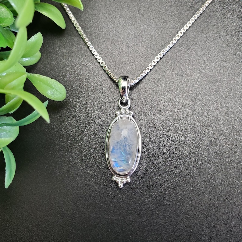 May include: A silver chain necklace with a silver oval pendant featuring a white moonstone.