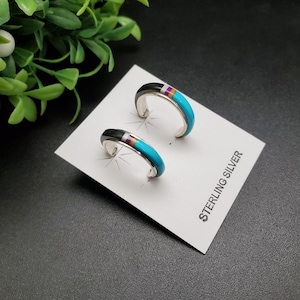 Puede incluir: Un par de pendientes de aro de plata de ley con incrustaciones de turquesa, negro y morado. Los pendientes están sobre una tarjeta blanca con el texto "STERLING SILVER".