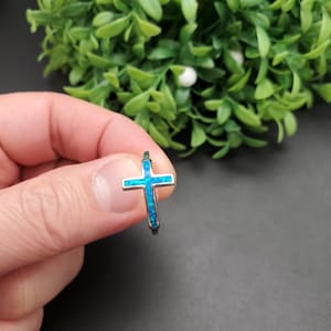 May include: A silver ring with a blue opal cross design.