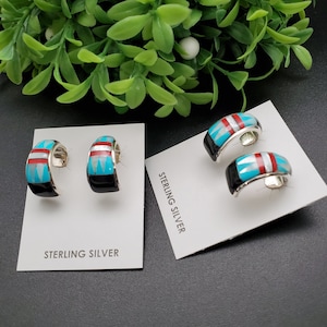 May include: A pair of sterling silver hoop earrings with turquoise, red, and white inlay. The earrings are displayed on a white card with the words "Sterling Silver" printed on it.