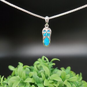 Op de afbeelding: Een zilveren ketting met een blauwe opaal hanger in de vorm van een flip-flop.